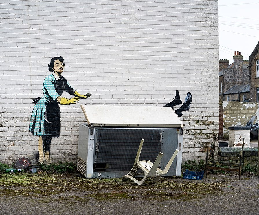 a brick wall with a painting of a woman standing next to a refrigerator