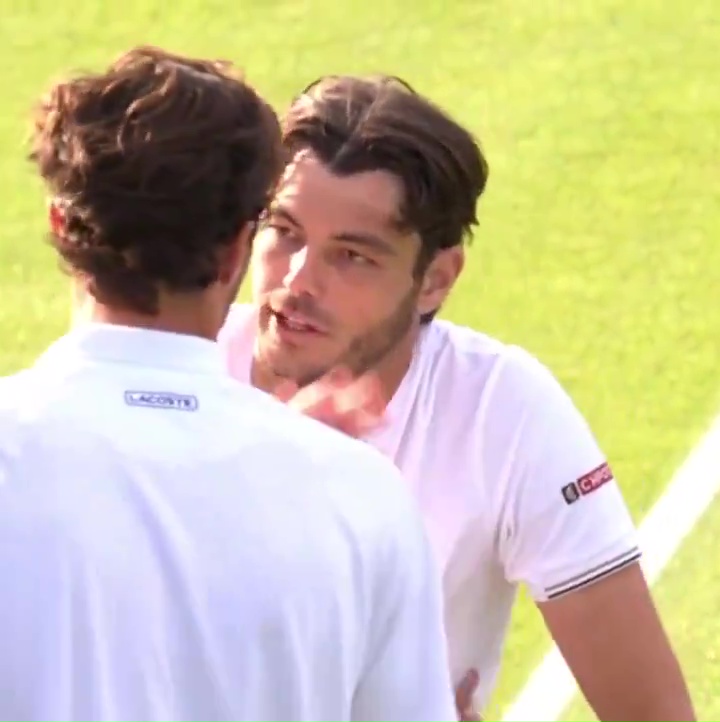 a man wearing a white lacoste shirt talks to another man