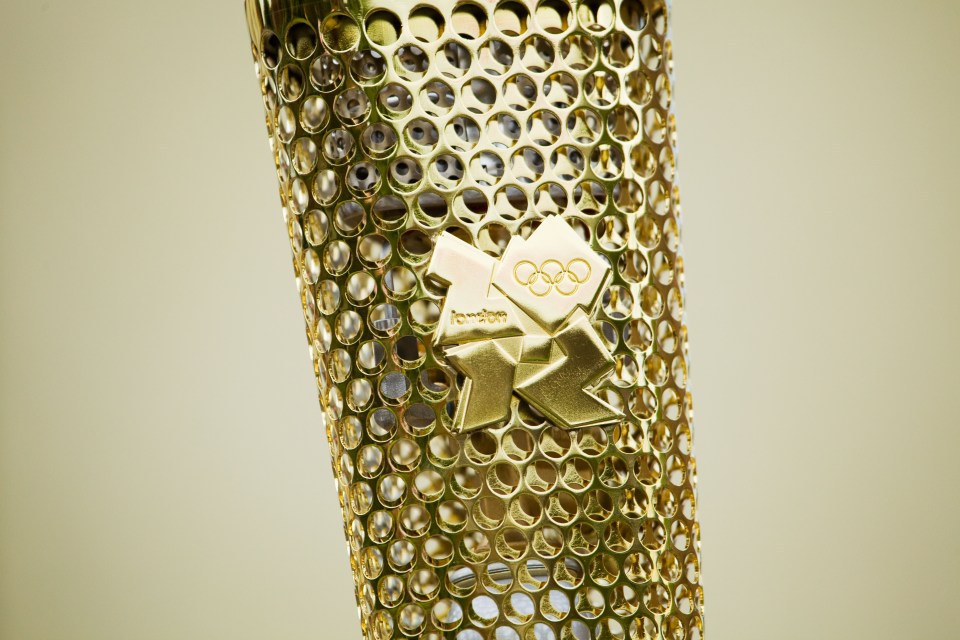 A close-up photograph of a London 2012 Olympic Torch showing the 2012 logo.