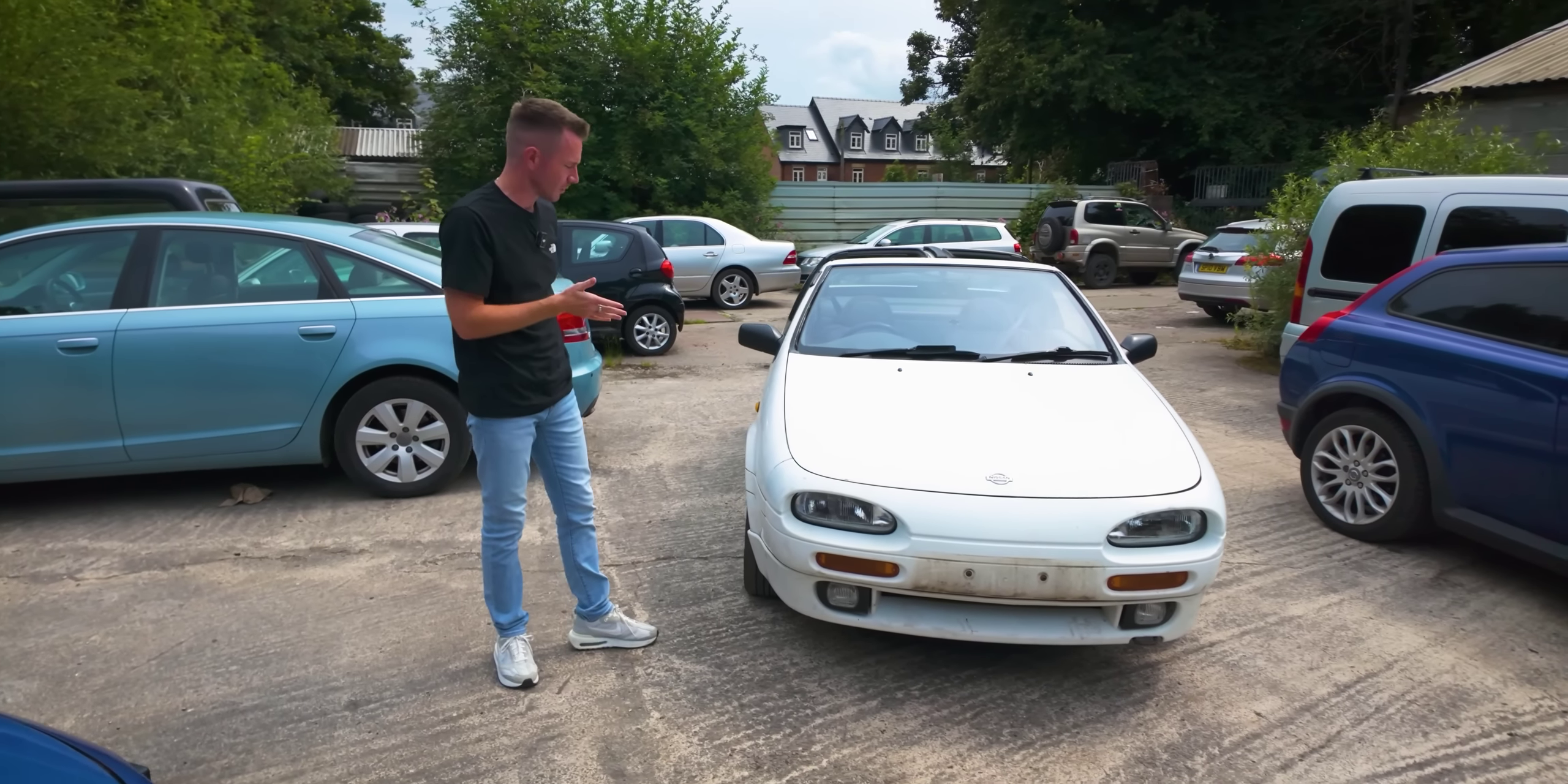 a man stands next to a white car in a parking lot