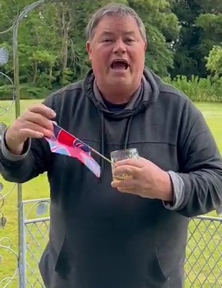 a man is holding a flag and a glass of whiskey .