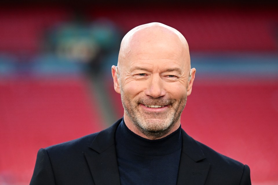 a bald man in a suit and turtleneck smiles for the camera