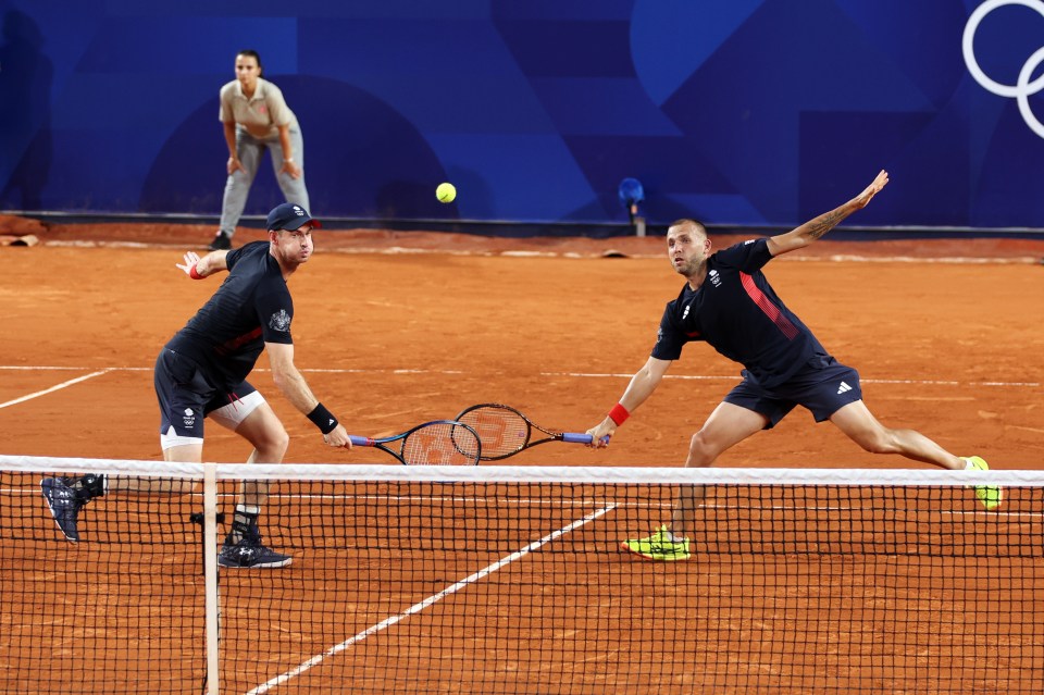 two men are playing tennis on a court with a referee watching