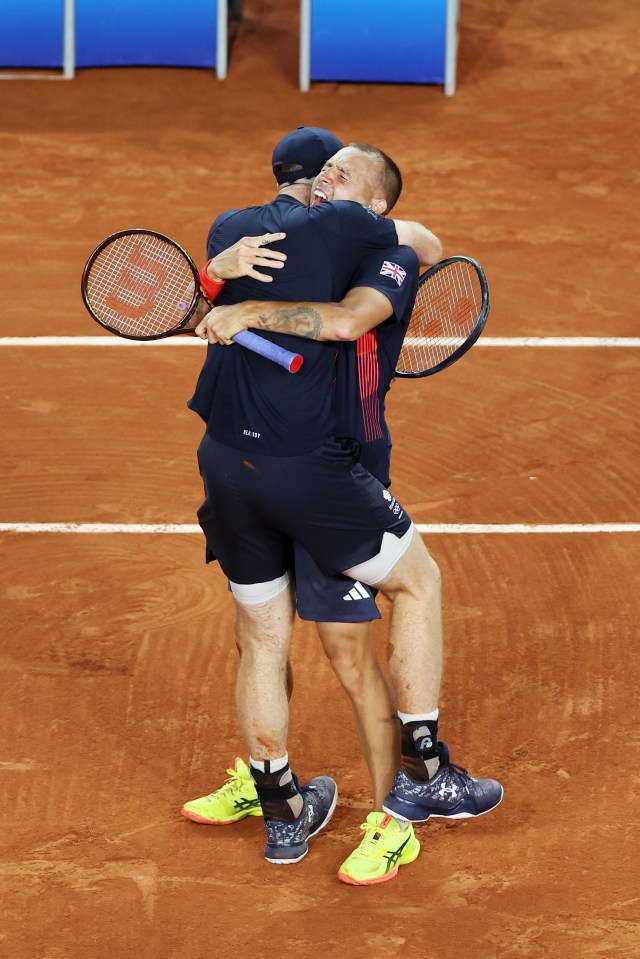 two men hugging on a tennis court with one wearing a shirt that says wilson