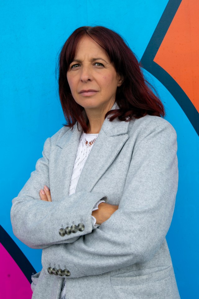 a woman in a grey coat stands with her arms crossed