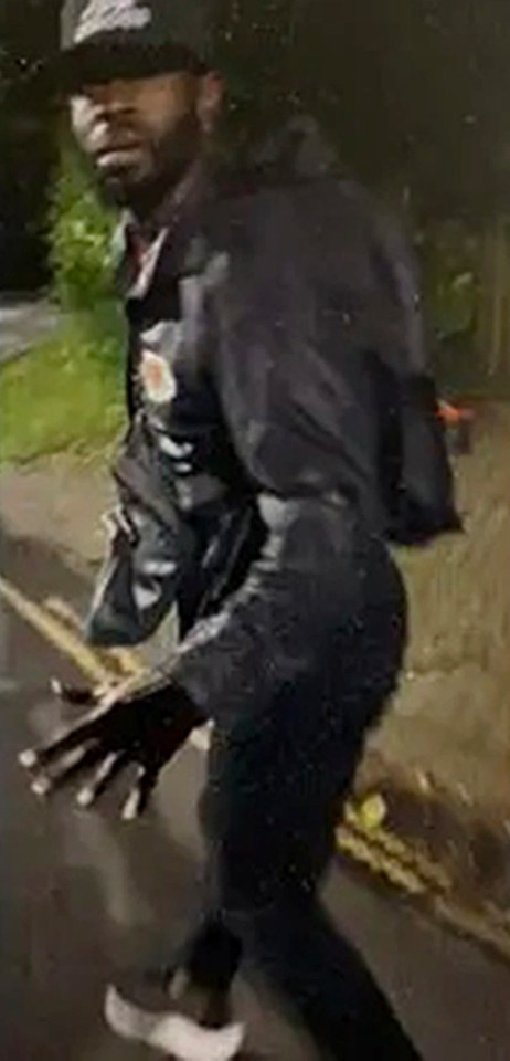 a man in a black jacket and hat is walking down the street at night .