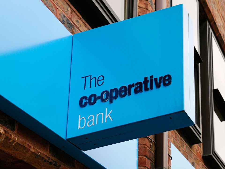 a blue sign for the co-operative bank hangs from the side of a building