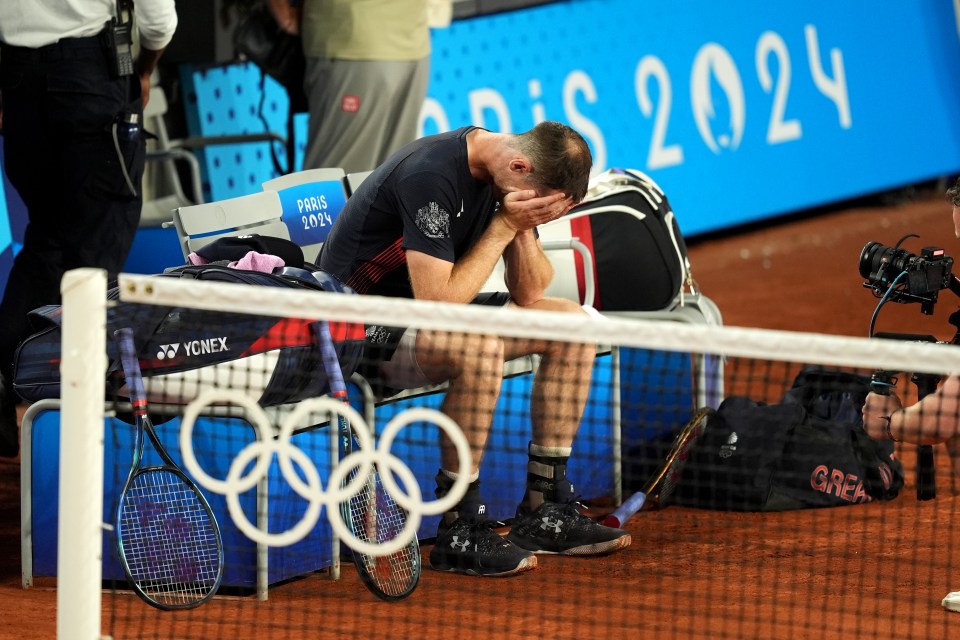 a man sits on a bench with his head in his hands in front of a sign that says paris 2024