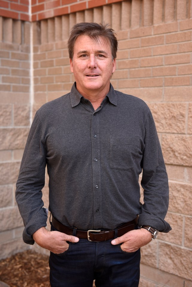 a man with his hands in his pockets stands in front of a brick wall