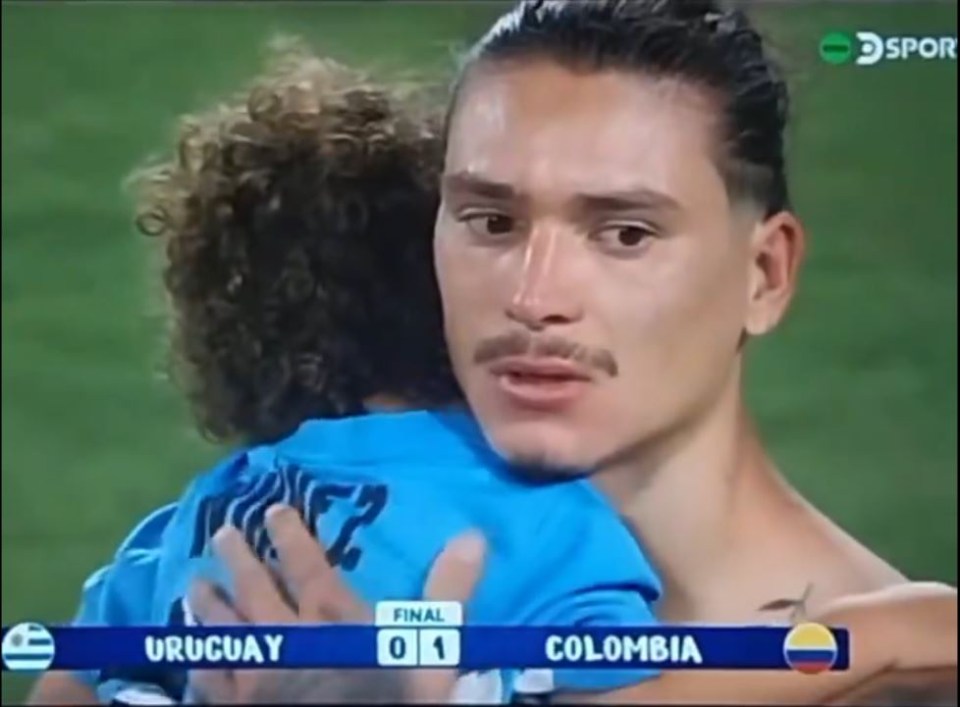 a man is hugging a child in front of a scoreboard that says uruguay and colombia