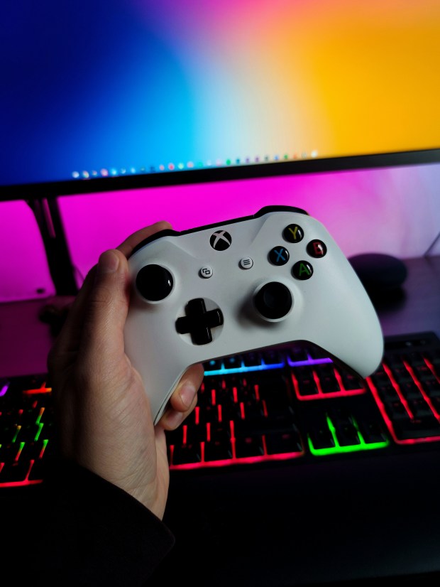 a person holding an xbox controller in front of a keyboard