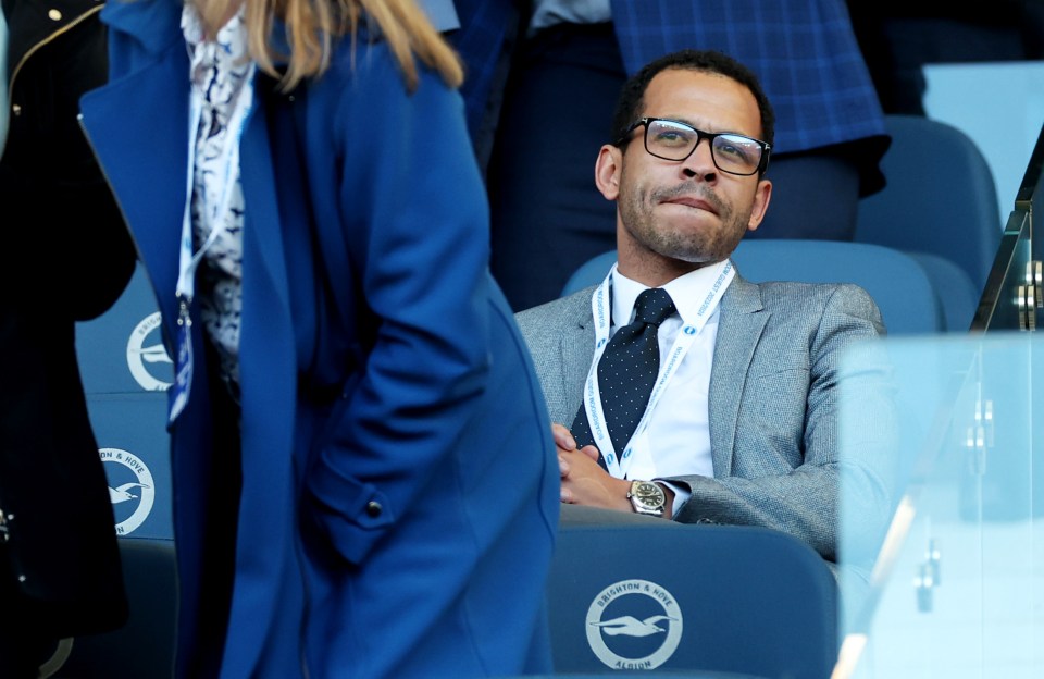 a man in a suit sits in a stadium with a blue seat that says brighton & hove