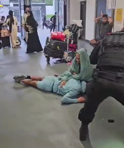 a man is laying on the floor in an airport while a woman holds him .