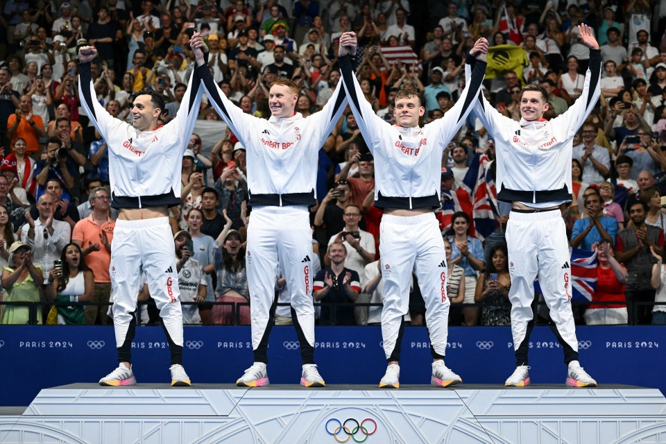 four athletes stand on a podium with the olympic rings in the background