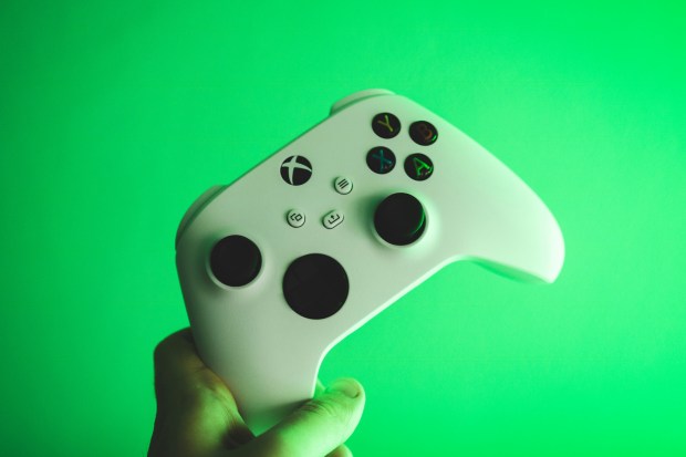 a person is holding a white xbox controller in front of a green background