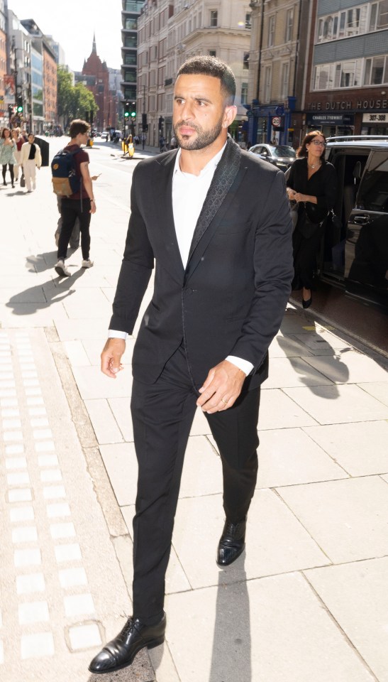 a man in a black suit is walking down a sidewalk