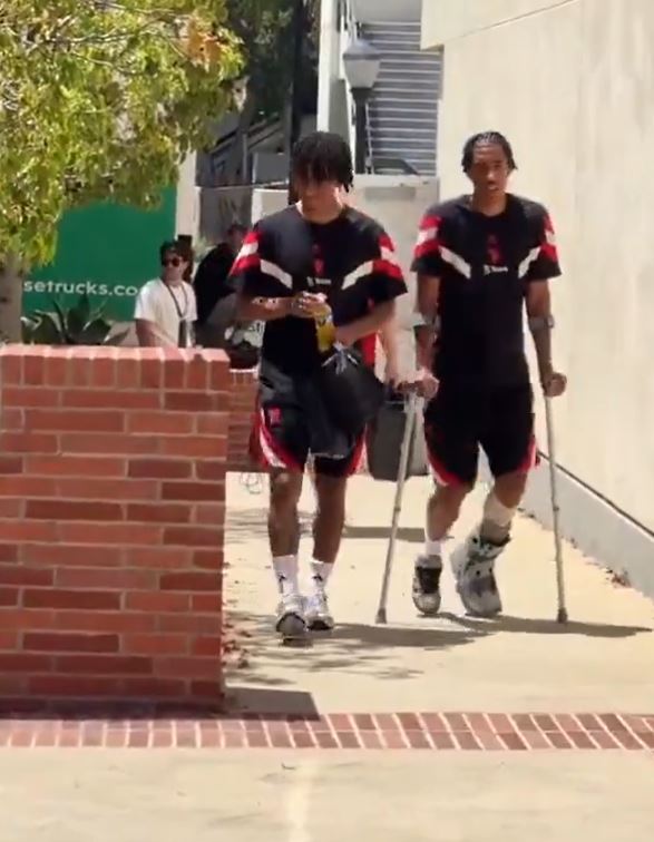 two men are walking down a sidewalk with crutches .