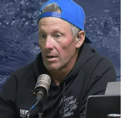 a man wearing a blue hat and a black hoodie is sitting in front of a microphone .