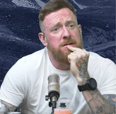 a man with a beard and tattoos is sitting in front of a microphone .