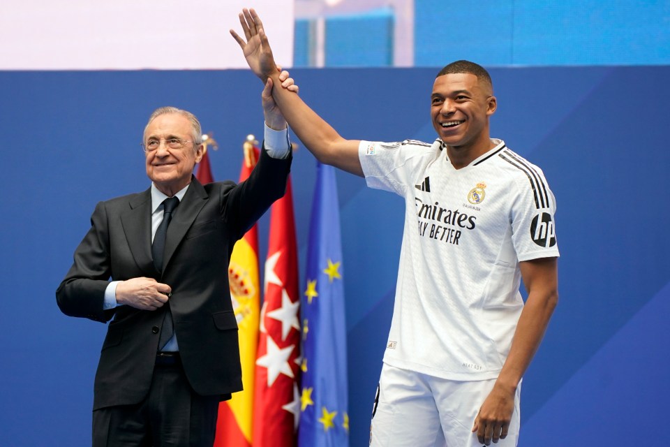 a man in a suit stands next to a man in a white emirates fly better jersey