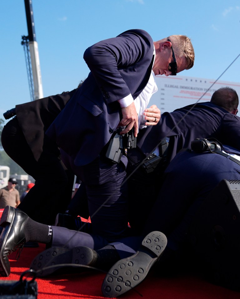 A Secret Service agent draws out his gun next to Trump as they dive for cover