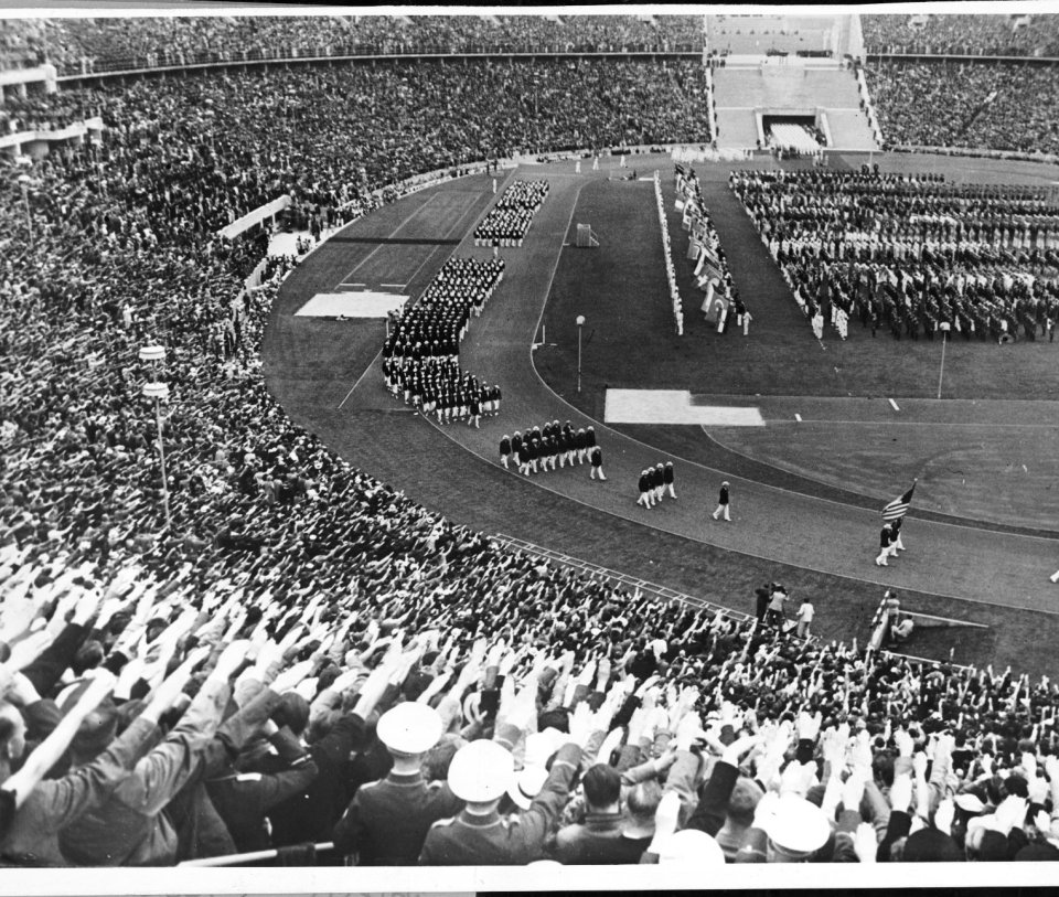 a black and white photo of a stadium full of people saluting