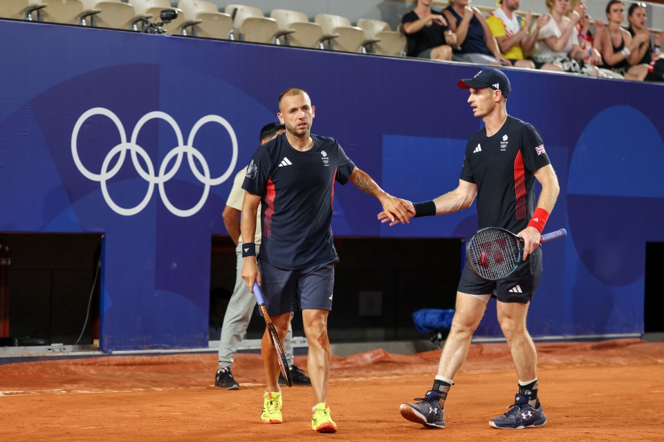 two men shake hands in front of an olympic sign