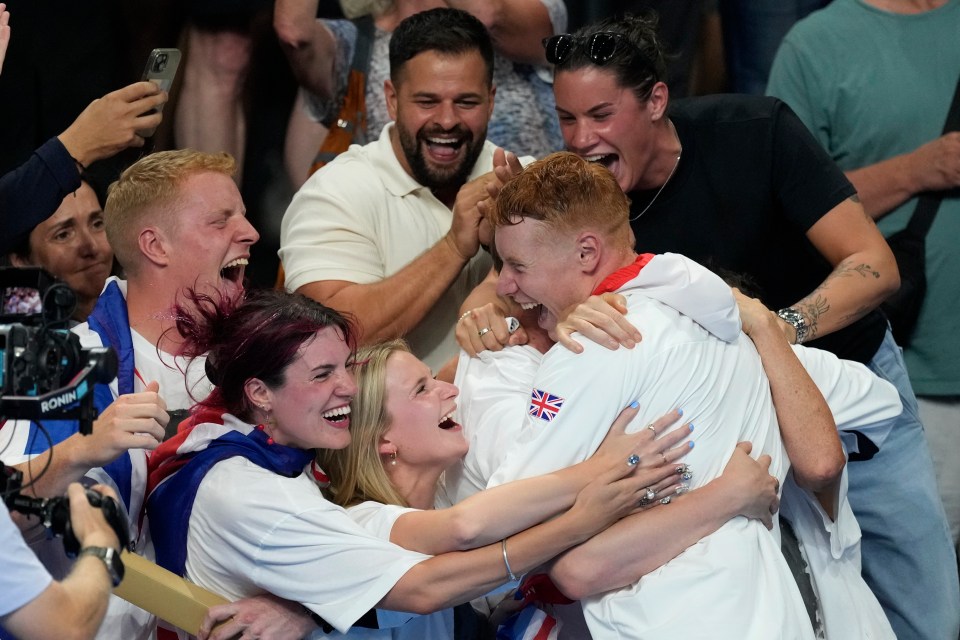 a group of people hugging a man with a british flag on his shirt