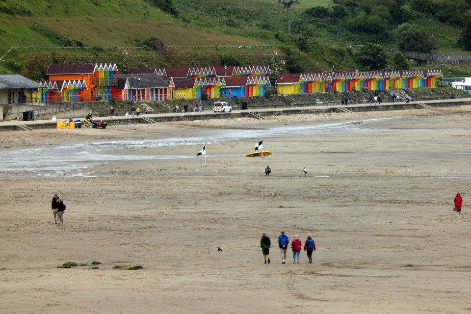 a group of people walking on a beach in front of colorful huts