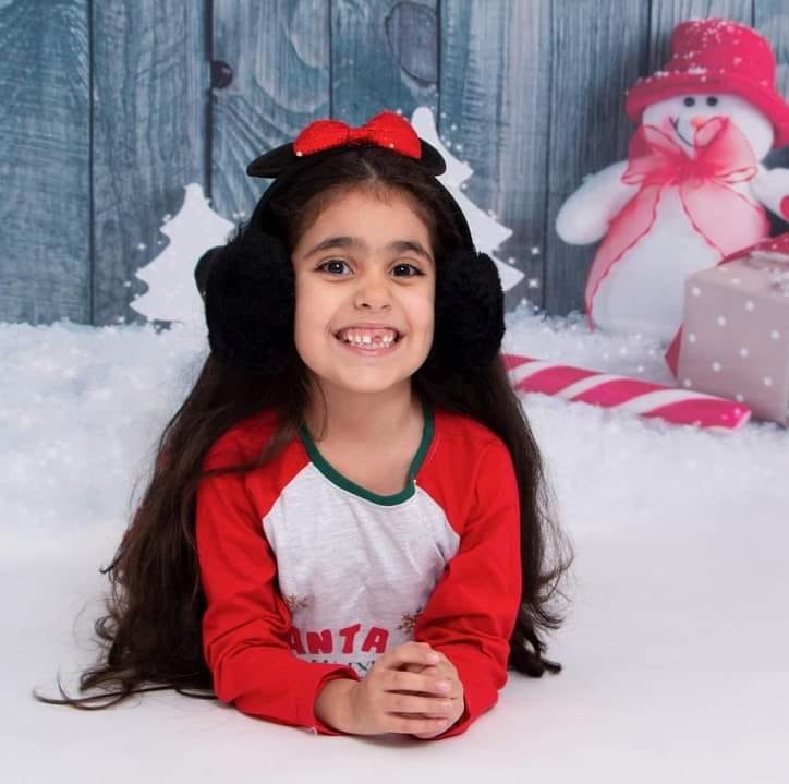 a little girl wearing ear muffs and a santa shirt