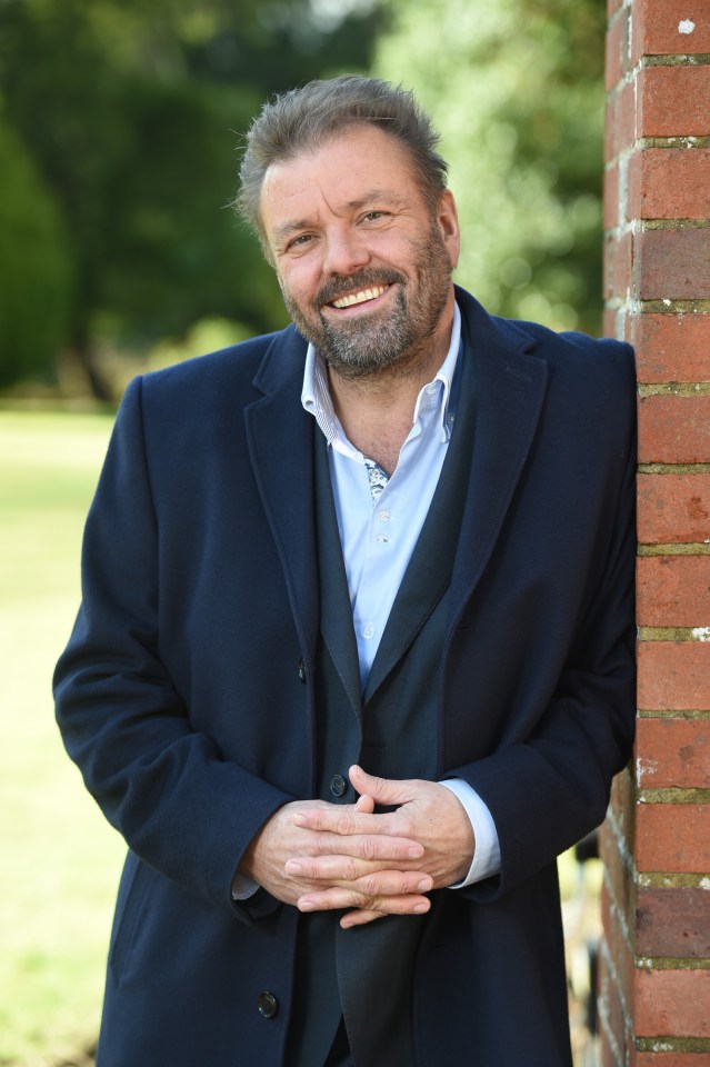 a man leaning against a brick wall with his hands folded