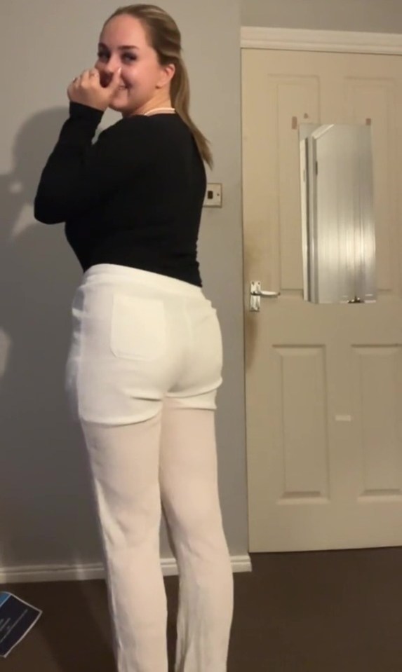 a woman in a black top and white pants stands in front of a door