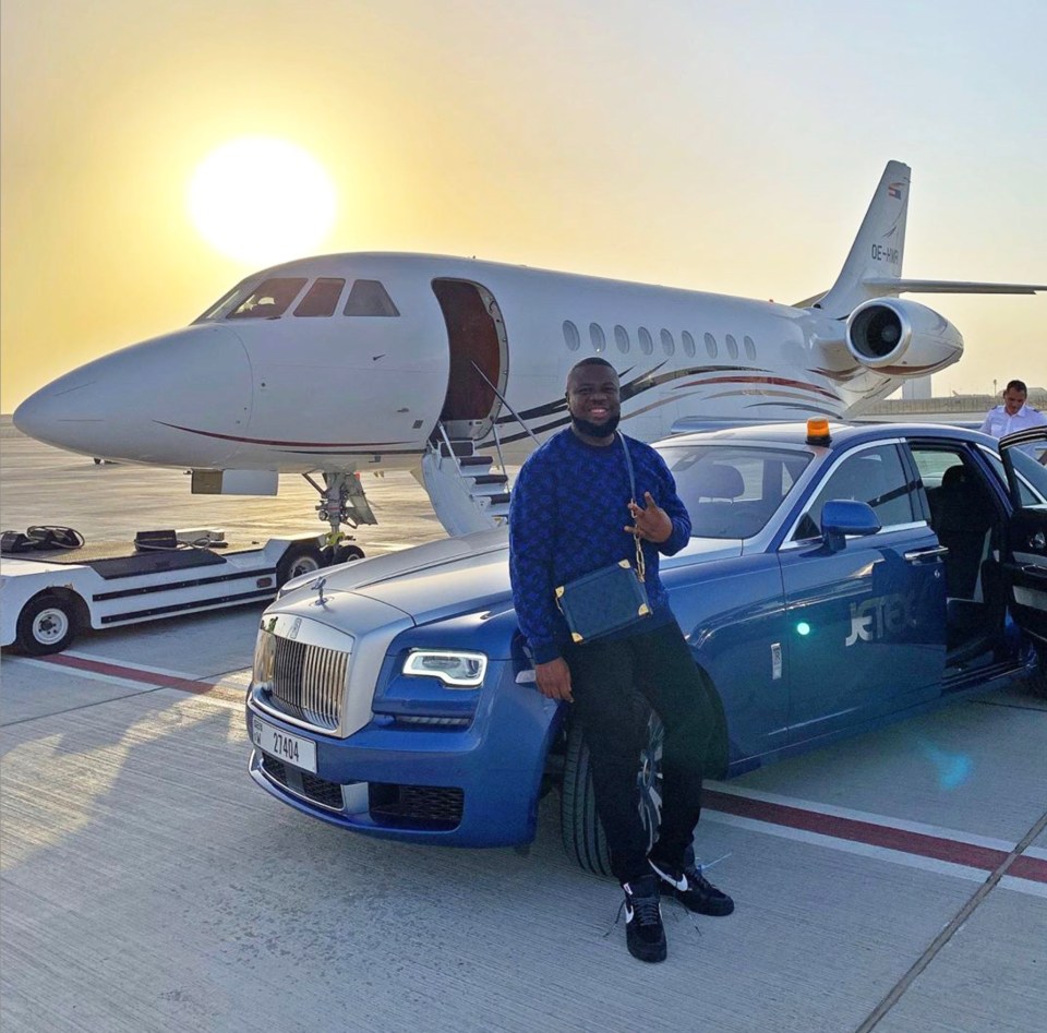 a man stands next to a blue rolls royce and a private jet