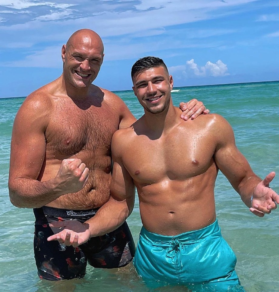 two men are posing for a picture in the water and one of them is wearing a pair of budweiser shorts