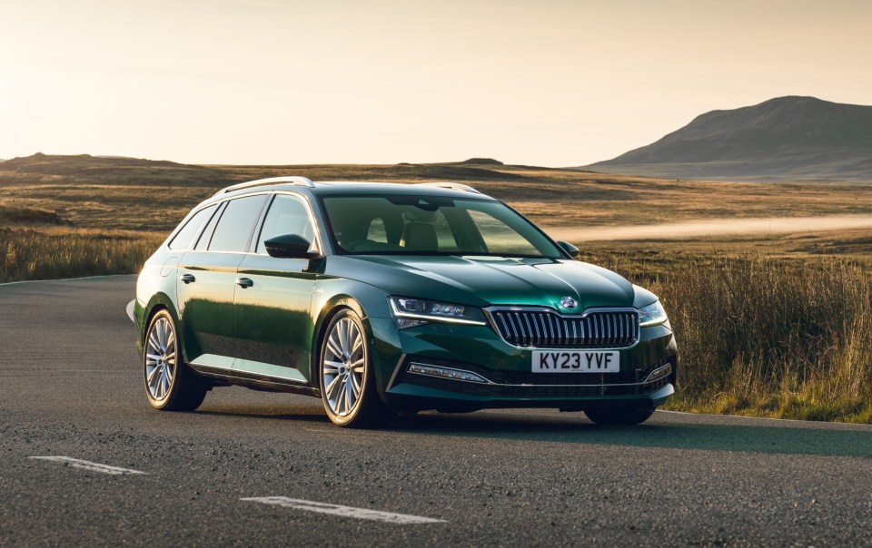 a green skoda is driving down a road with mountains in the background