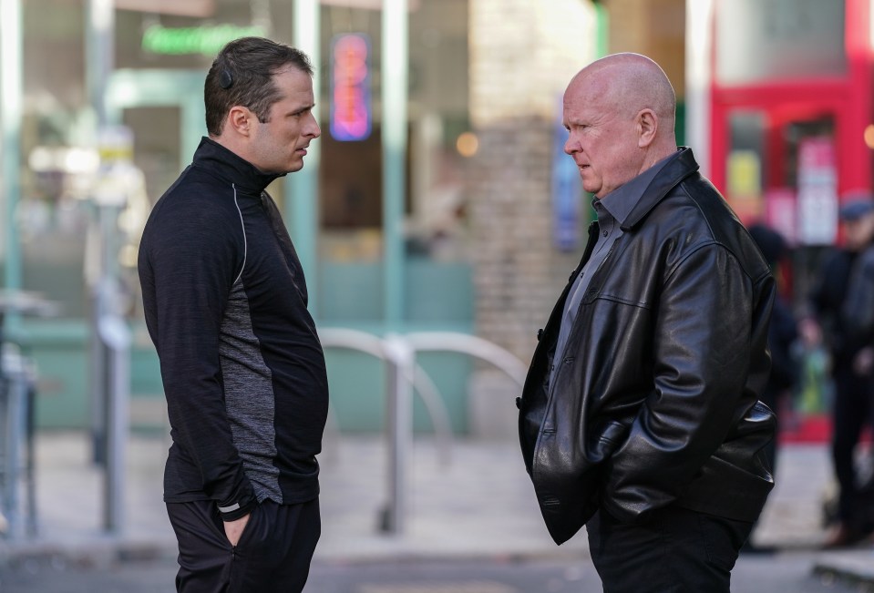 two men are standing in front of a store with a sign that says ' open ' on it