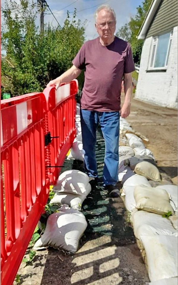 a man in a purple shirt stands next to a pile of sandbags