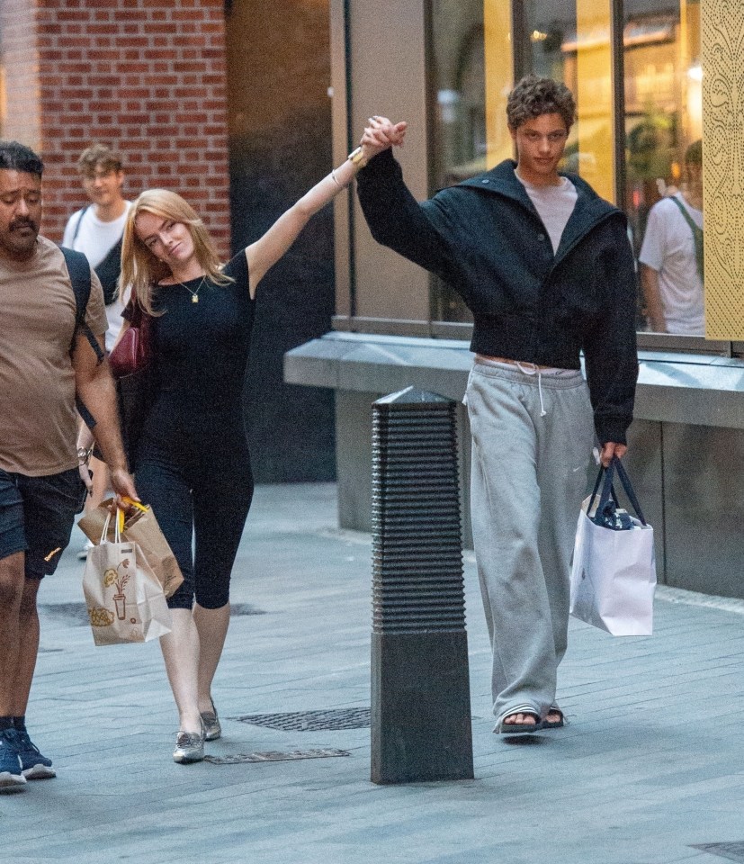 a woman holds a man 's hand as they walk down the street