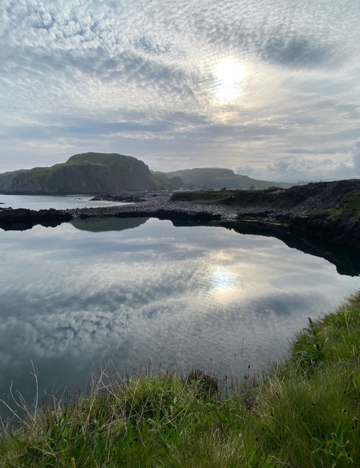 a body of water with mountains in the background and the sun shining through the clouds