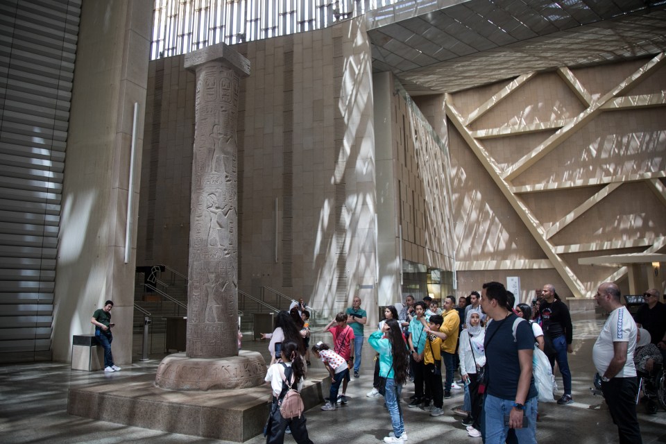 Visitors gather in front of an obelisk during a guided tour of the main hall of the Grand Egyptian Museum