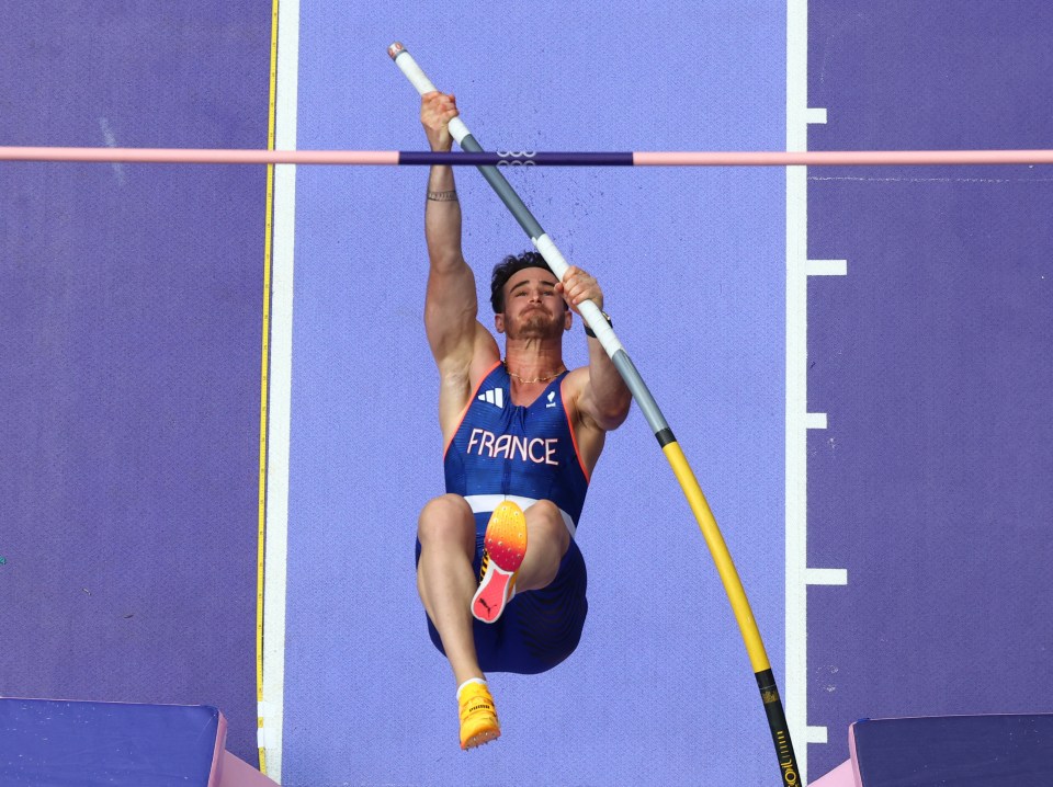 a man in a france shirt is jumping over a bar