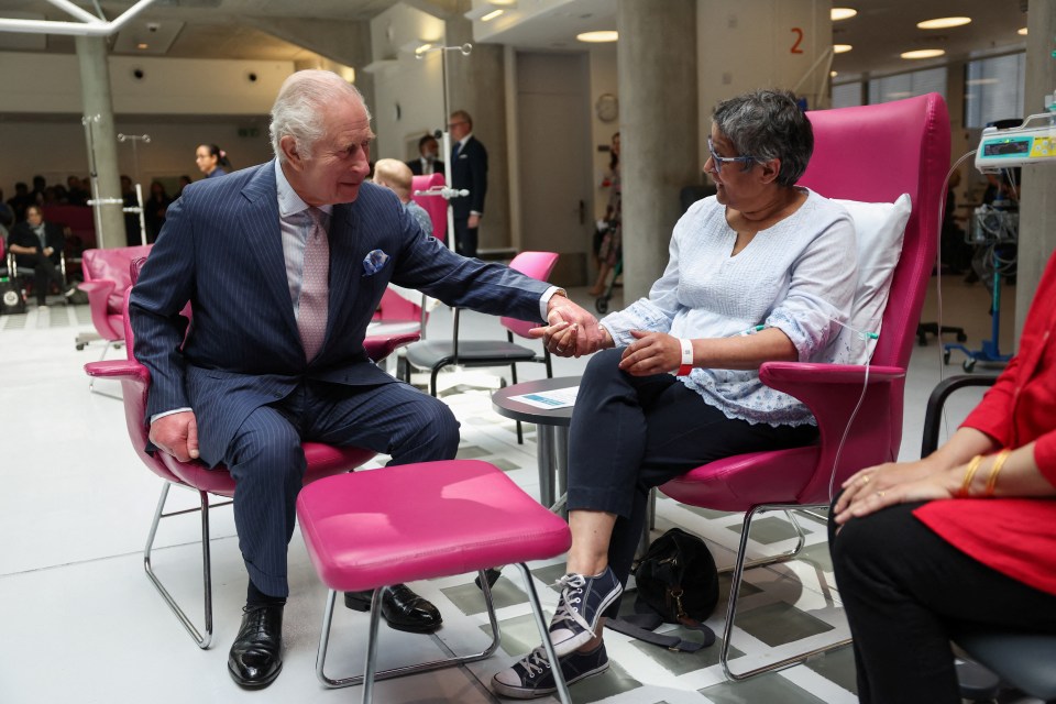 a man in a suit shakes hands with a woman in a pink chair