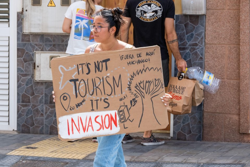 a woman holding a sign that says it 's not tourism it 's invasion