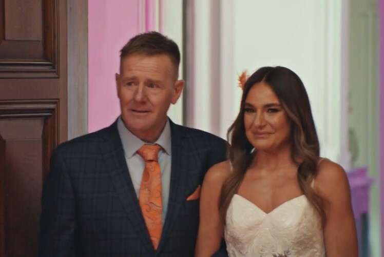 a man in a suit and tie stands next to a woman in a wedding dress