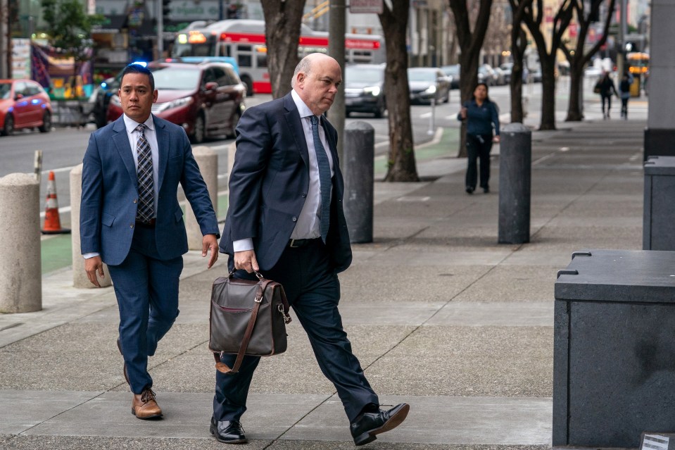 a man in a suit walks down a sidewalk next to another man