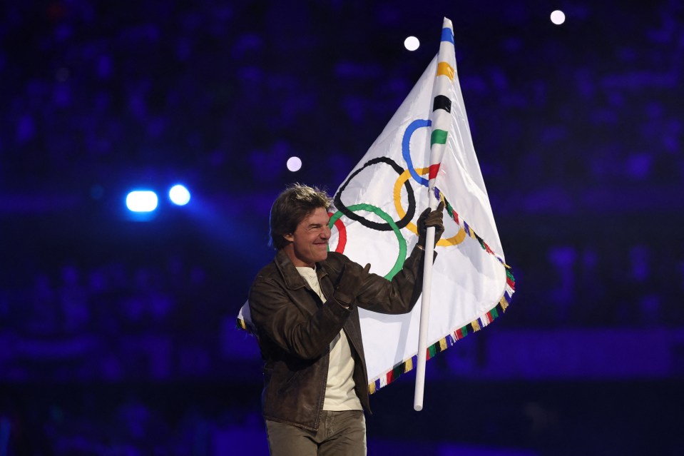 a man in a brown jacket is holding an olympic flag