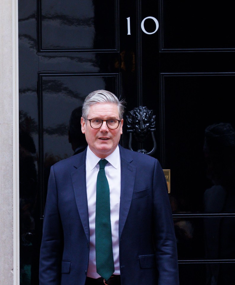 a man in a suit and tie stands in front of a black door with the number 10 on it