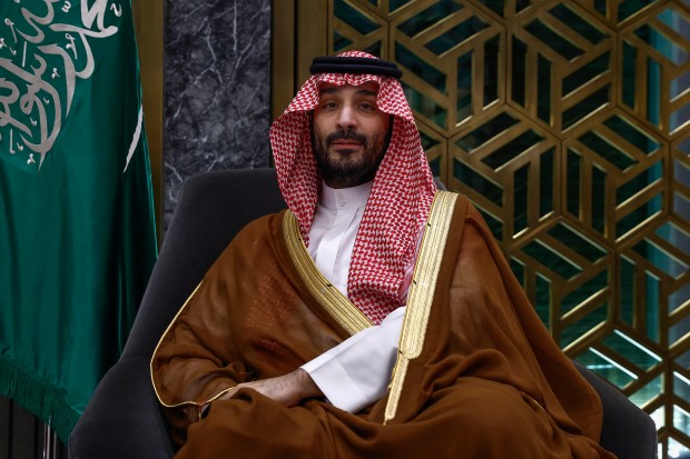 a man in a traditional costume sits in front of a green and white flag