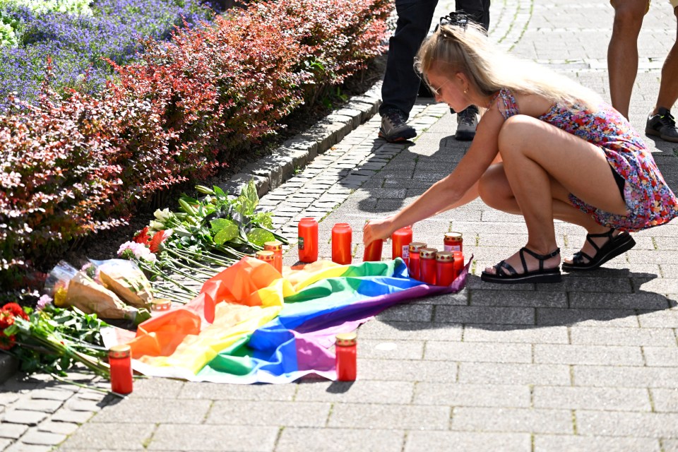 a woman kneeling down in front of a rainbow flag and candles