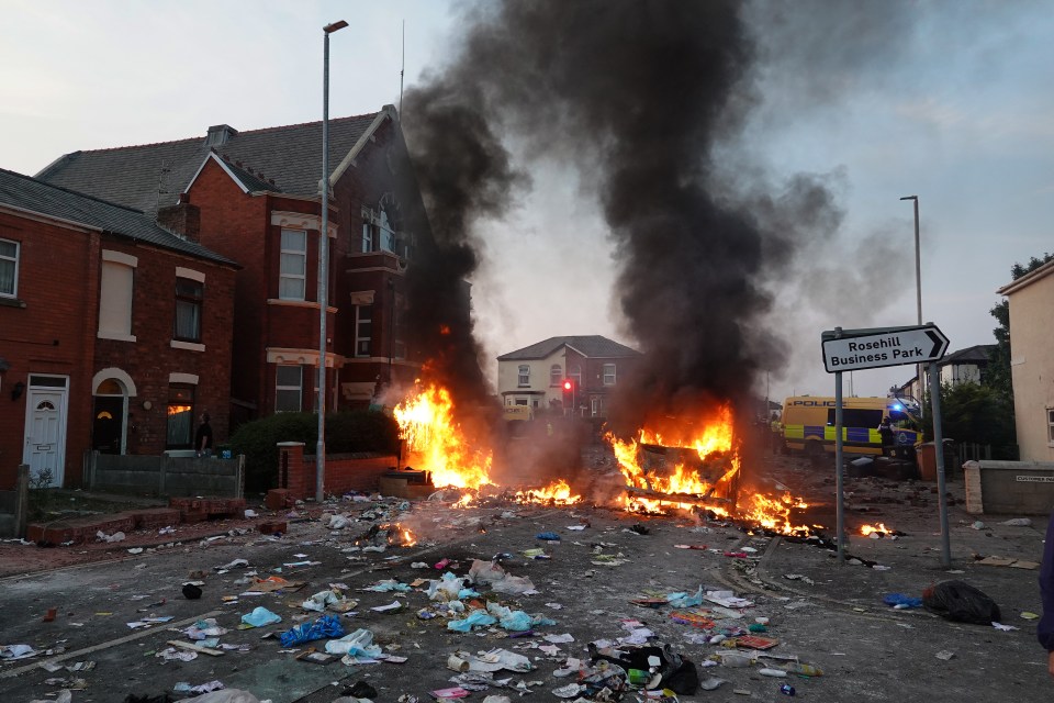 Riot police hold back protesters near a burning police vehicle after disorder broke out in Southport on July 30